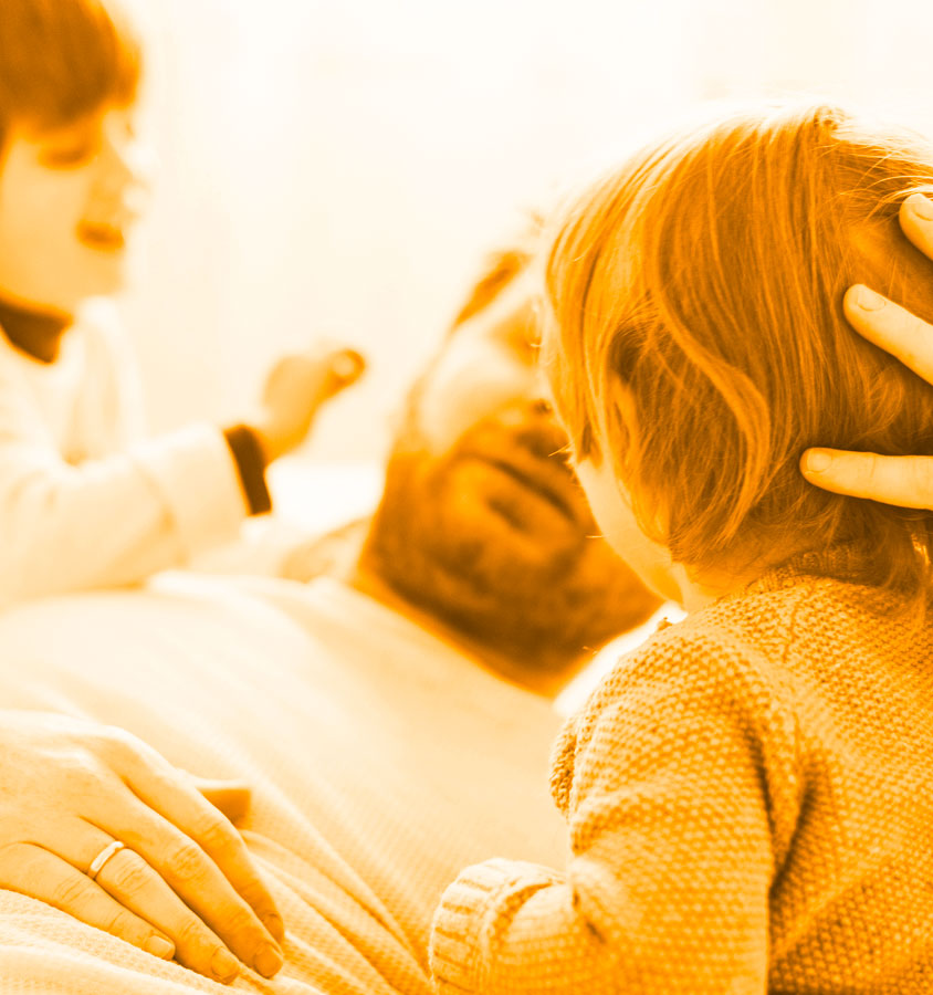 Genitore stanco sdraiato con i suoi figli piccoli che giocano e gli dimostrano affetto, simbolo dell’amore familiare nonostante la fatica